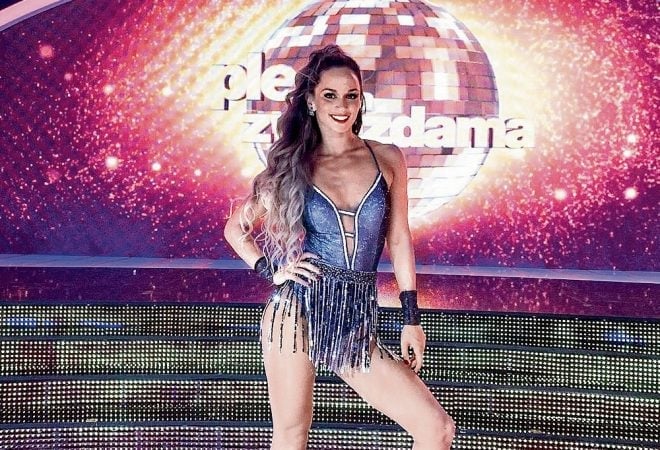 Tina Walme u plavom plesnom kostimu sa šljokicama i resama pozira ispred svjetleće disco kugle i pozadine s natpisom Ples sa zvijezdama