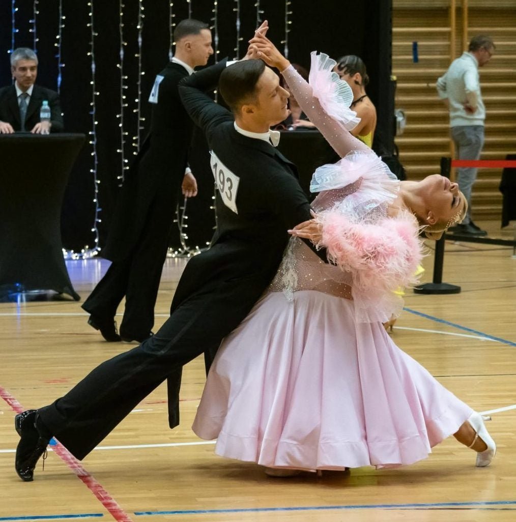 Male and female ballroom dancers performing a dramatic dip move on a wooden dance floor during a competition