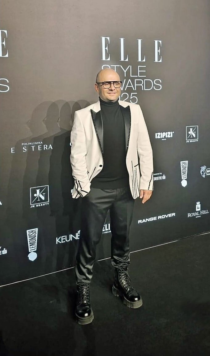Man in white blazer and black turtleneck at Elle Style Awards 2025 event, standing on red carpet with sponsor logos