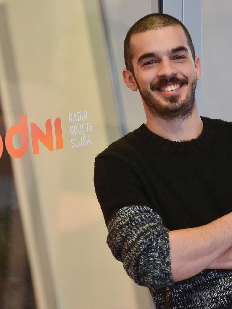 Marko Bratoš, hrvatski radijski voditelj i natjecatelj Plesa sa zvijezdama 2026., smije se u crnoj majici ispred studija radija s logotipom 'Radio koji te sluša'