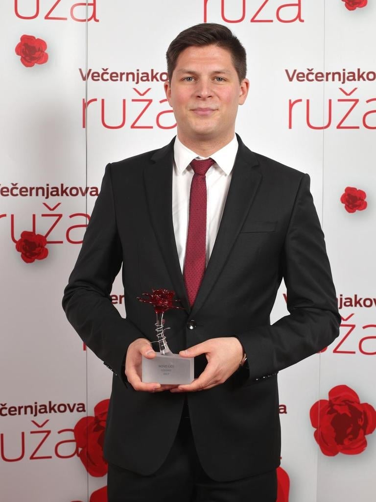 Ivan Dorian Molnar, sportski novinar i voditelj HRT-a, u crnom odijelu s bordo kravatom drži nagradu Večernjakova ruža za novo lice godine 2018.